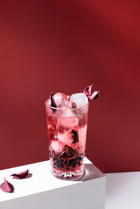 Composition of glass filled with pink gin tonic and ice placed on white table against red background