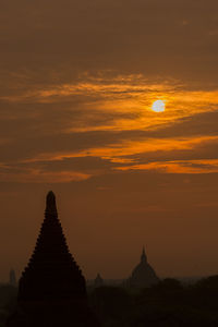 Silhouette stupas against dramatic sky during sunset