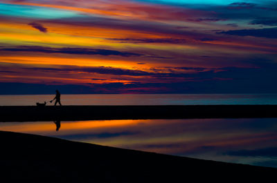 Silhouette person by sea against sky during sunset