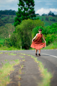 Young woman wearing sunglasses walking on road against trees in forest