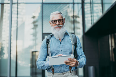 Senior hipster holding digital tablet against building