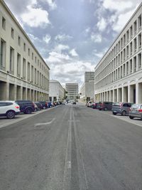 Road passing through city against cloudy sky