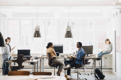 Male and female computer engineers working against window in creative office