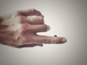 Close-up of hand holding cigarette against white background