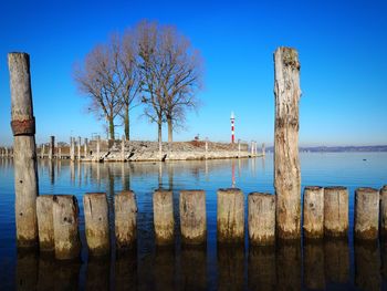 Wooden posts on sea against clear blue sky