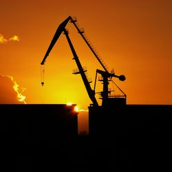 Silhouette of cranes against sky during sunset