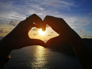 Midsection of man making heart shape against sky during sunset