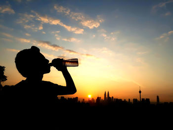Silhouette man drinking water against sky during sunset
