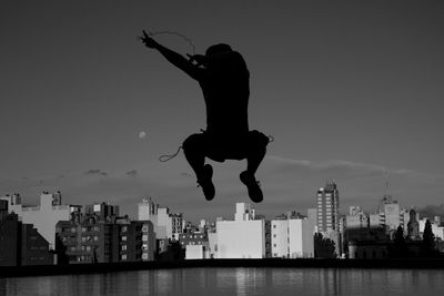 Silhouette man jumping against cityscape at dusk