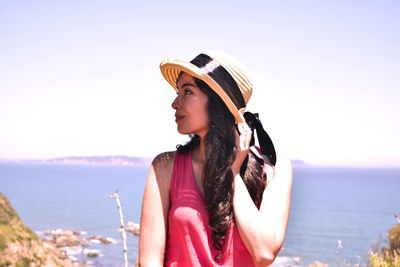 Young woman wearing hat standing at beach against clear sky