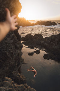 Woman on rock at beach against sky during sunset