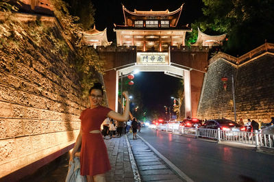 Young woman flexing muscles while standing on sidewalk in city at night