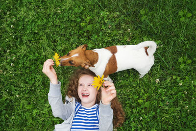 Laughing girl enjoy playing with her puppy dog on the grass in the summer park.