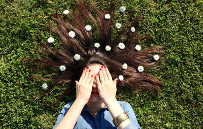 Woman lying on grass covering eyes with flowers in hair