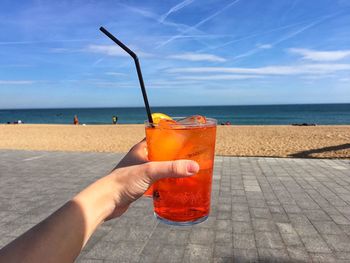 Cropped image of hand holding aperol spritz in glass at beach