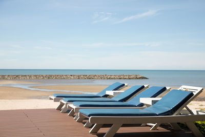 Empty chairs on beach against sky