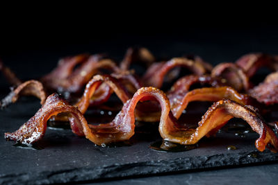 Close up of wavy strips of crispy maple pepper bacon against a dark background.