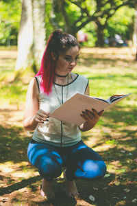 Woman reading file while crouching at park