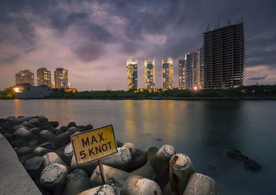 View of illuminated buildings by river against sky