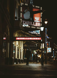 Rear view of people walking on illuminated road at night