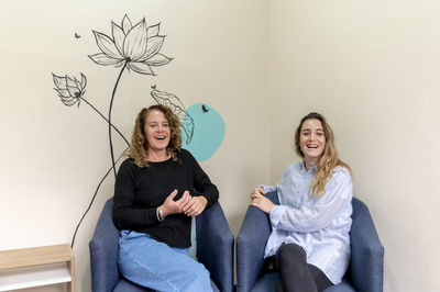 Female coworkers smiling while relaxing sitting on armchairs during a break at work.