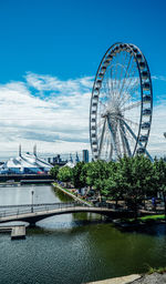 Ferris wheel by river against sky in city