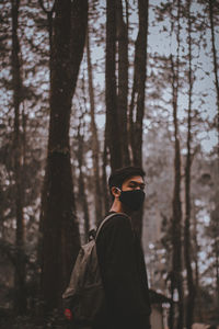 Man standing by tree trunk in forest