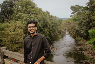 Portrait of young man standing against waterfall