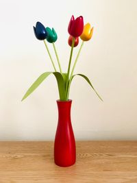 Close-up of red roses in vase on table against wall