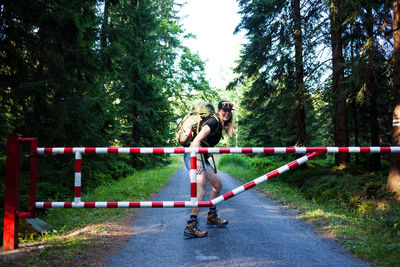 Portrait of cheerful woman with backpack standing on road in forest