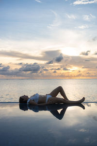 Woman lying down on a infinity pool at sunset in maldive islands