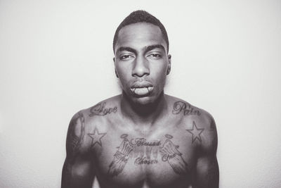 Portrait of shirtless mid adult man with tattoos standing against white background
