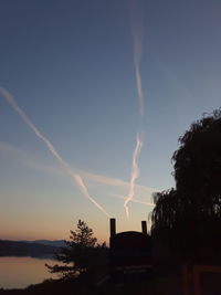 Low angle view of vapor trails over silhouette trees against sky