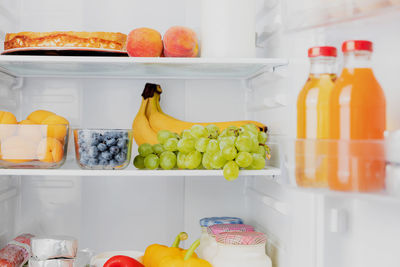 Front view of open two door fridge or refrigerator door filled with fresh fruits, vegetables, juice