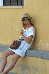 Portrait of woman eating lollipop while sitting on retaining wall outside house