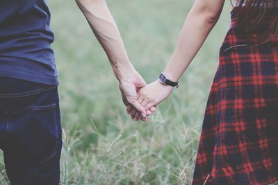 Midsection of couple holding hands while standing on field