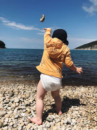 Rear view of person on rock at beach against sky