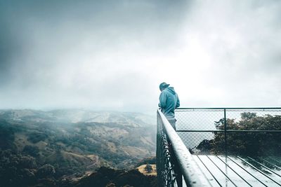 Man standing at observation point by landscape against cloudy sky