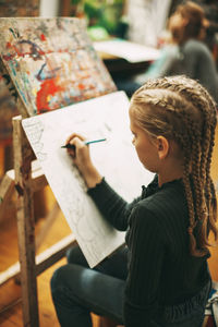 Beautiful teenage girl with pigtails at art school draws graphics with pen on easel, 