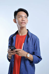 Potrait of handsome young asian man holding a smart phone and wear wristwatch with pretty smiling look at the copy space