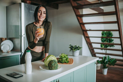 Smiling woman drinking juice in kitchen at home