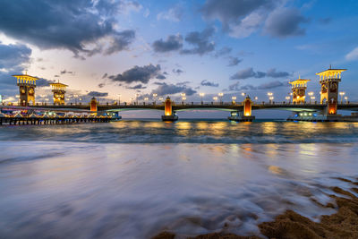 Illuminated bridge over sea against sky at night