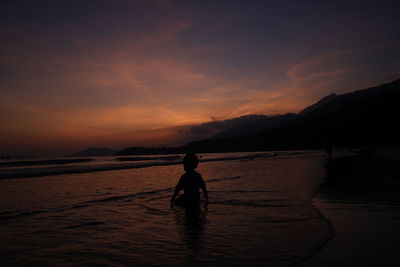 Silhouette man walking on beach against sky during sunset