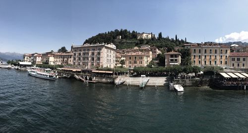 Boats moored on river by buildings against sky