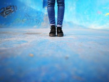 Low section of woman standing on street against blue wall