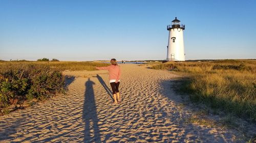 Rear view of woman on lighthouse by dune against sky