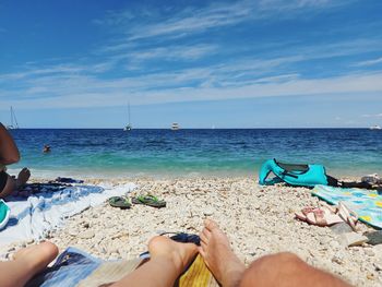 Low section of people relaxing on beach against sky