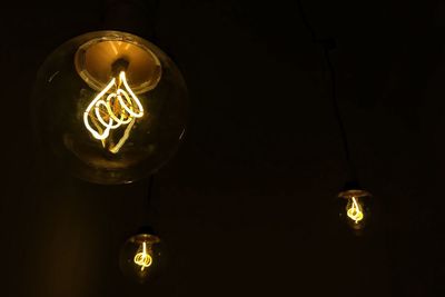 Low angle view of illuminated light bulbs hanging on ceiling