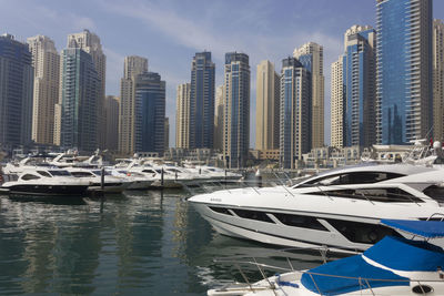 Boats moored in sea against modern buildings in city