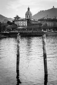 Wooden posts in river by building against sky